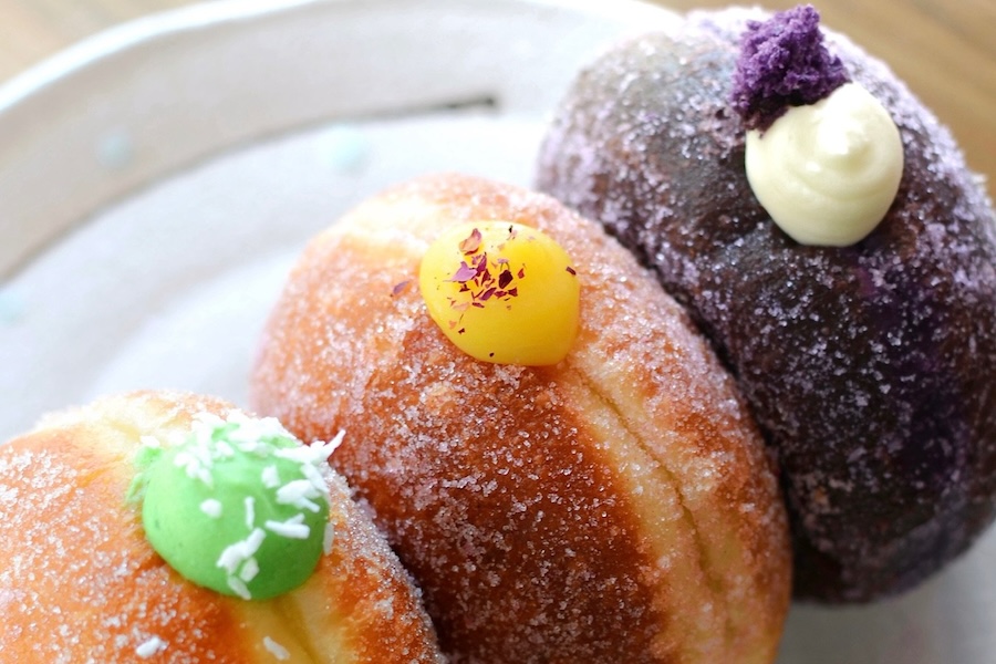 a trio of brioche donuts stuffed with ube, passionfruit and pandan sits on a plate