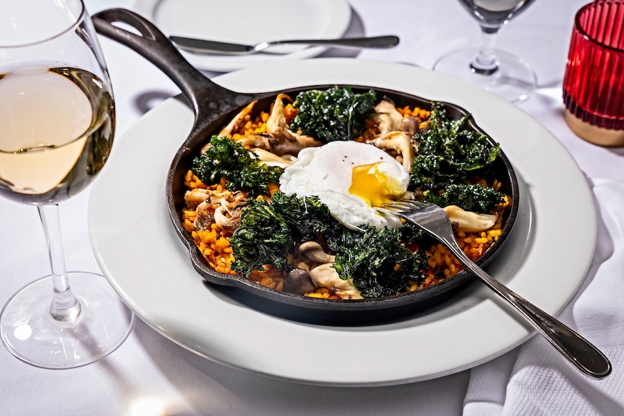 padella con paella, cavolo riccio e uova fresche su un tavolo bianco