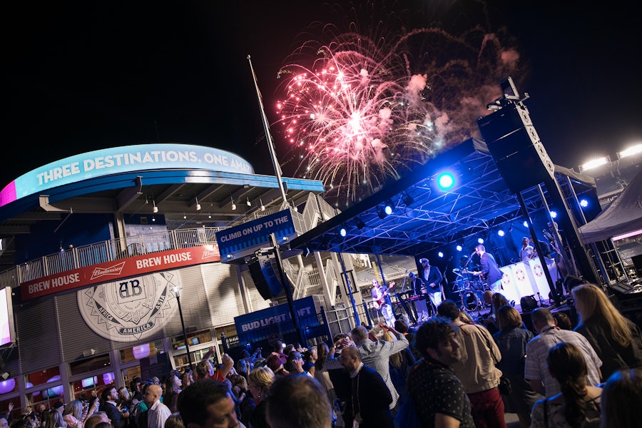 a crowd gathers to watch a music performance against a backdrop of fireworks