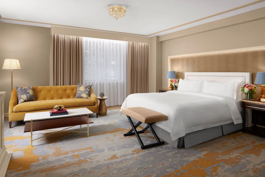 Luxurious hotel room with a king-size bed, sofa, and large window.