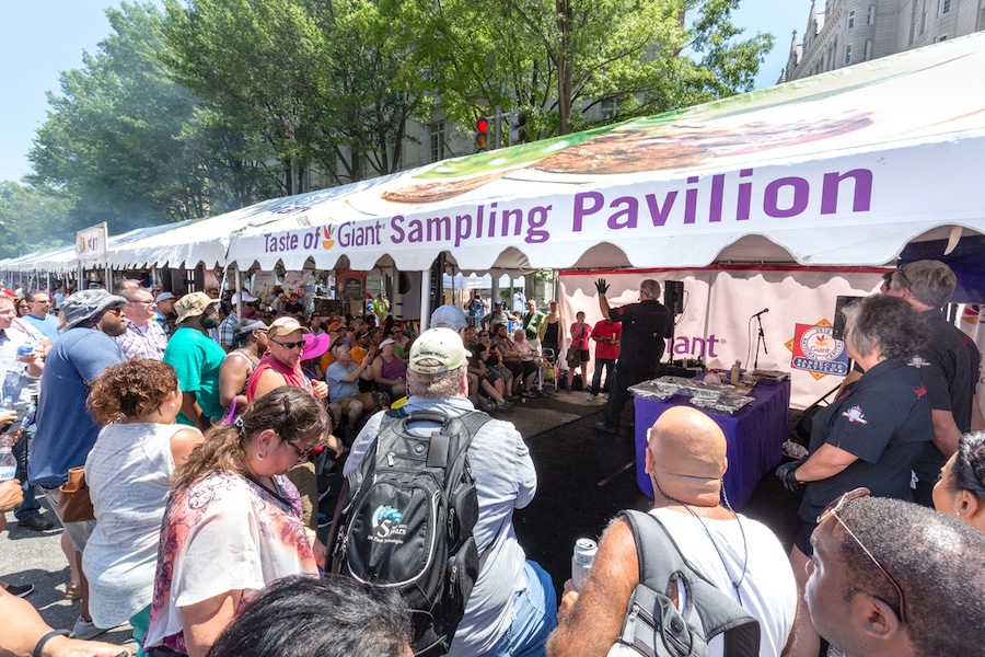 Sampling Pavilion: A large crowd gathered around a sampling pavilion at the Giant BBQ Battle, watching a cooking demonstration under a white tent.