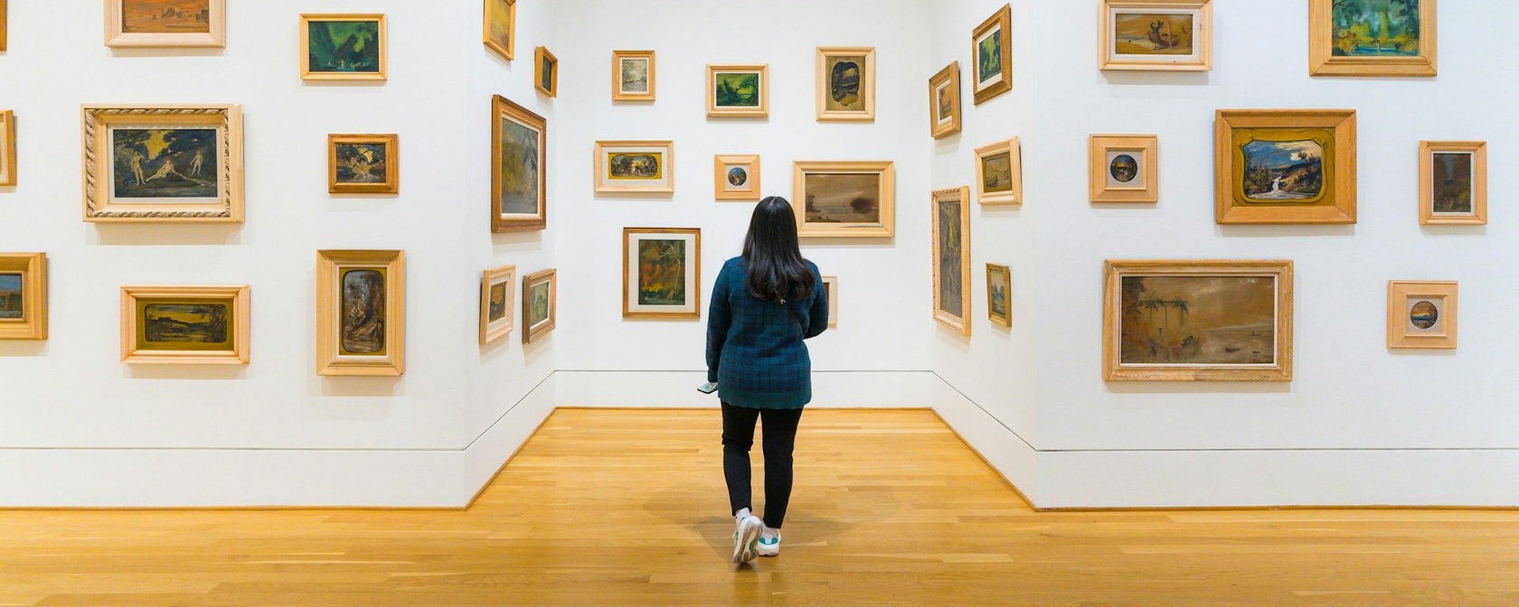 Ein Besucher erkundet eine Galerie der Phillips Collection, wo kleine gerahmte Gemälde in verschiedenen Stilen auf weißen Wänden angeordnet sind und so ein umfassendes Kunsterlebnis schaffen.