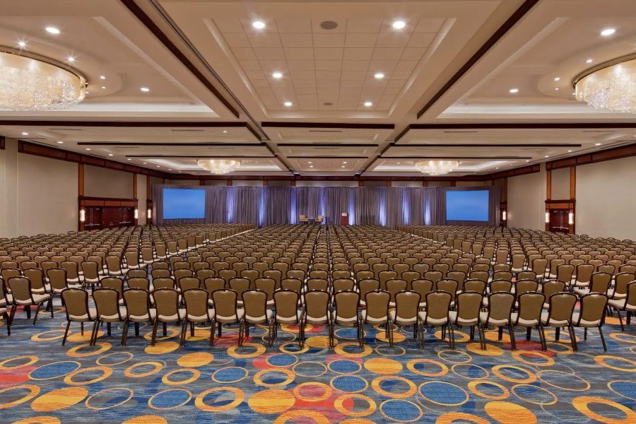 A large ballroom set up in theater style with rows of chairs facing a stage with projection screens and draped backdrops.