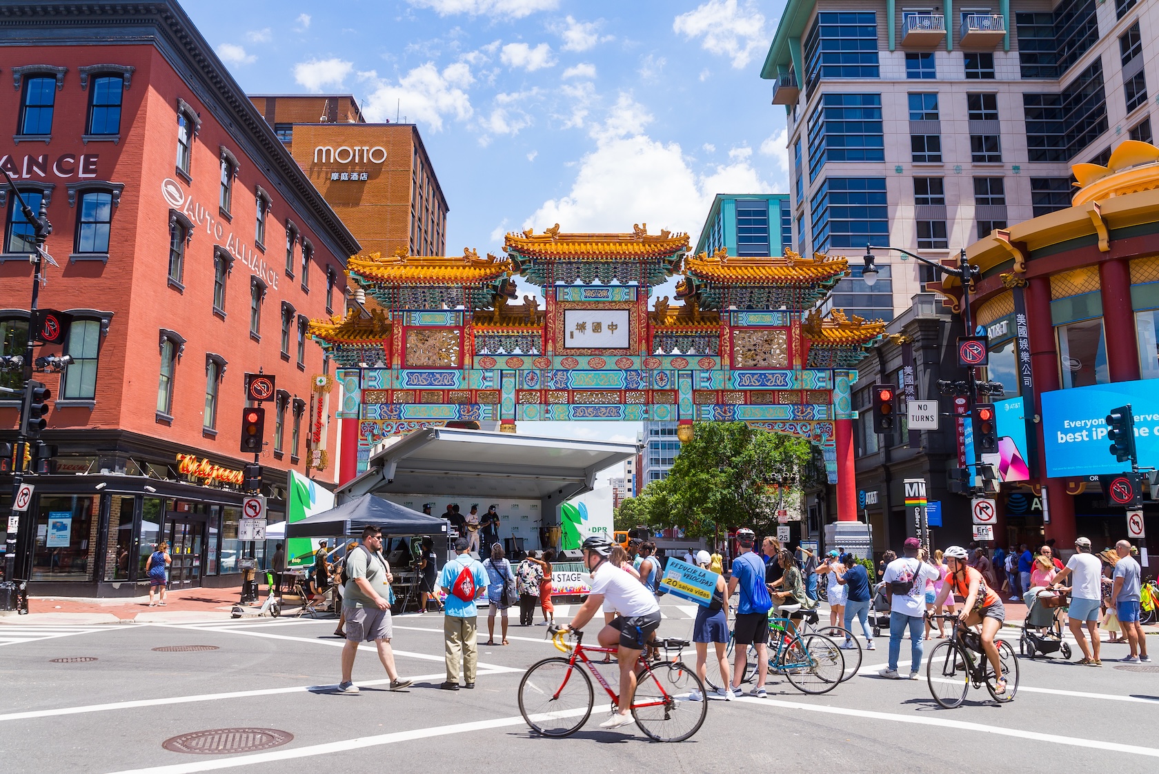 People walk and bike through a lively street festival beneath the colorful Friendship Archway in Washington, DC.