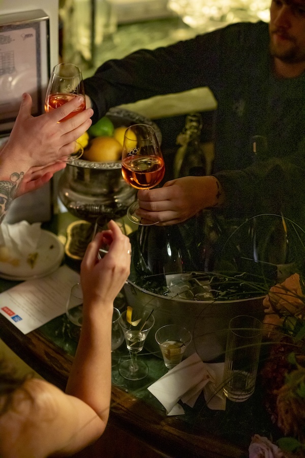 Guests clink glasses of rosé wine over a dimly lit bar during an intimate evening in Washington, DC.