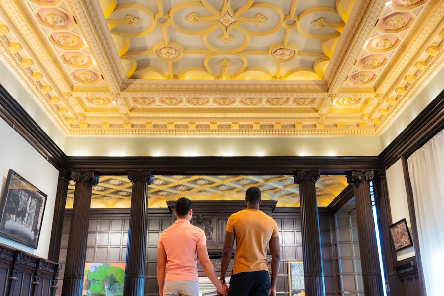 Two visitors stand hand in hand beneath an ornate, coffered ceiling inside The Phillips Collection.