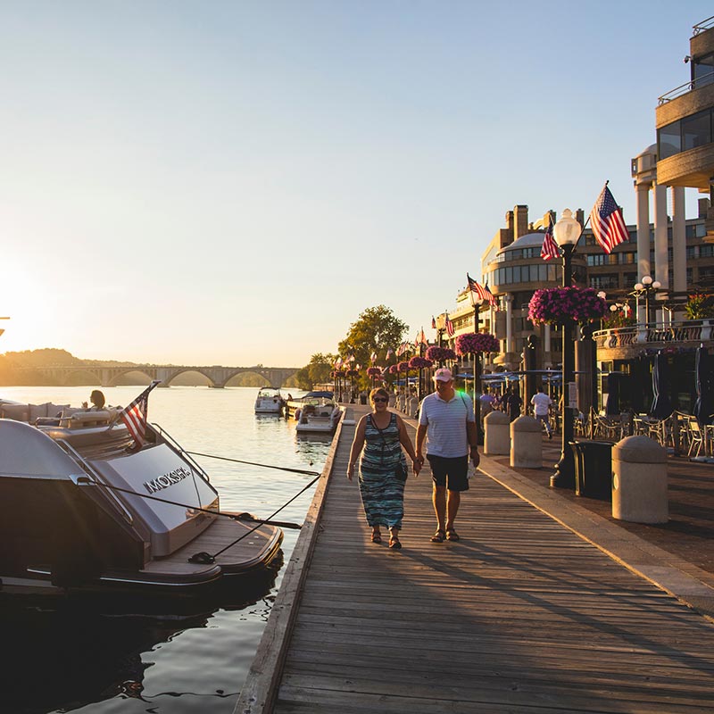 Couple walking along The Washington Harbour Georgetown Waterfront at sunset in Washington, DC
