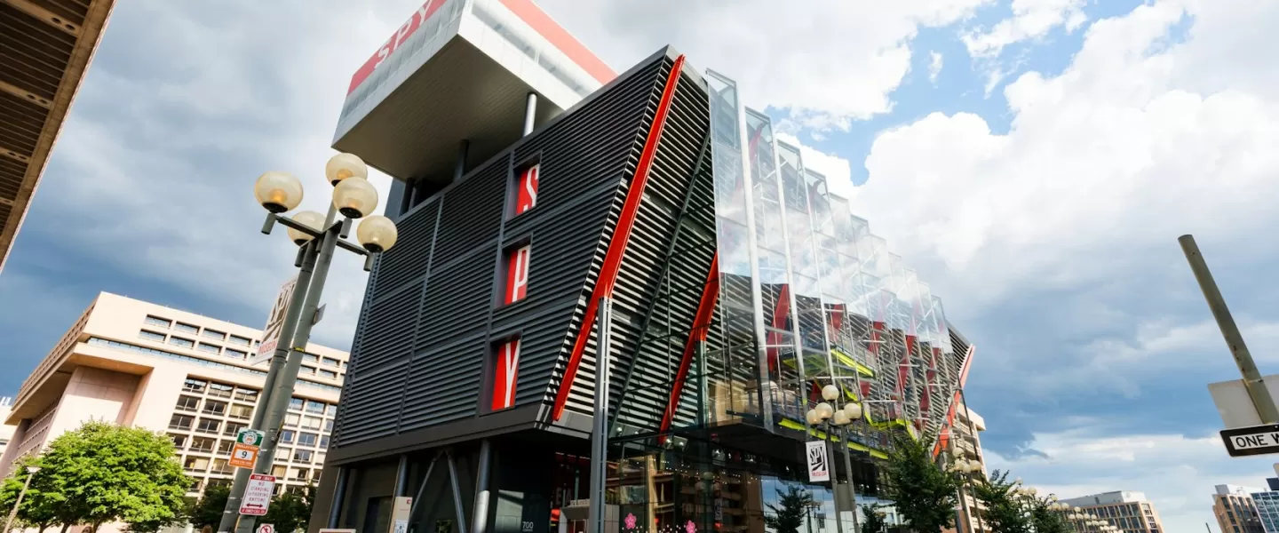 The modern exterior of the International Spy Museum in Washington, DC, featuring a striking design with red accents and glass panels under a cloudy sky.