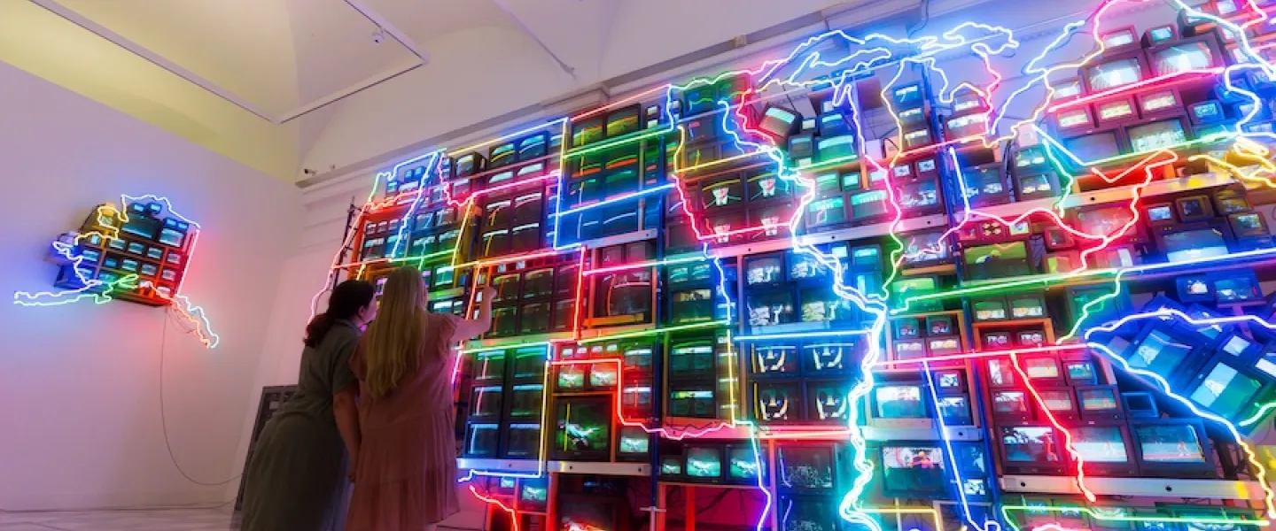 Two people look at a large, neon art installation that replicates the U.S.
