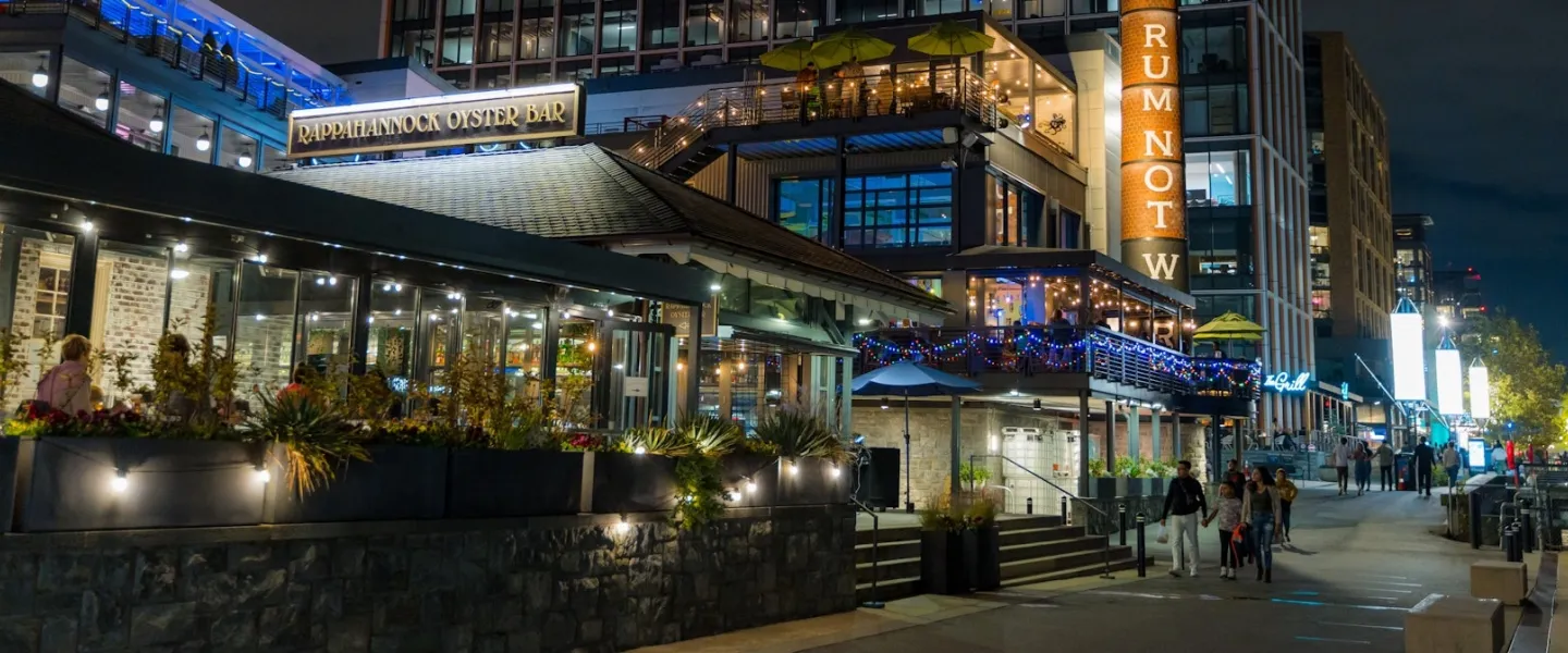 Businesses are lit up and busy at night along The Wharf in DC. 