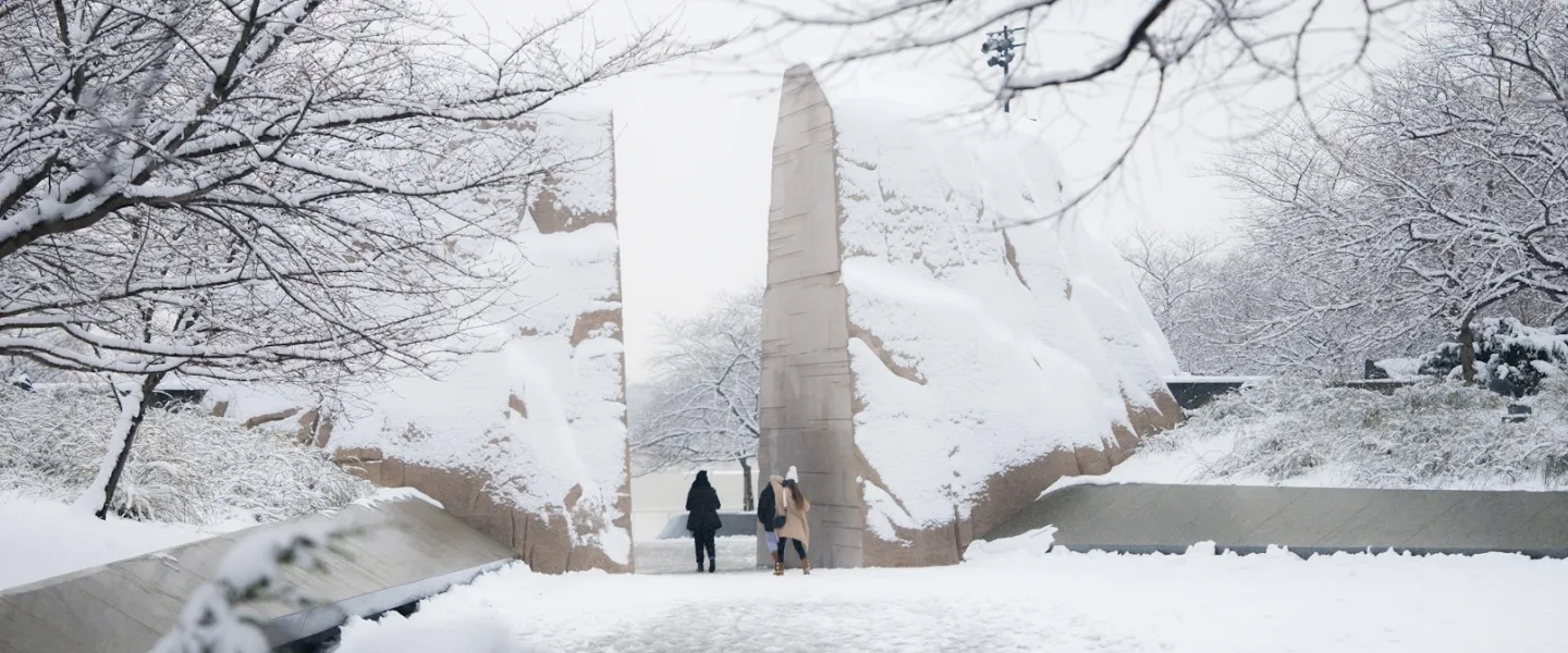 Visitors walk through the snow-covered entrance stones at the Martin Luther King, Jr. Memorial in Washington, DC surrounded by frosted trees after a winter snowfall.