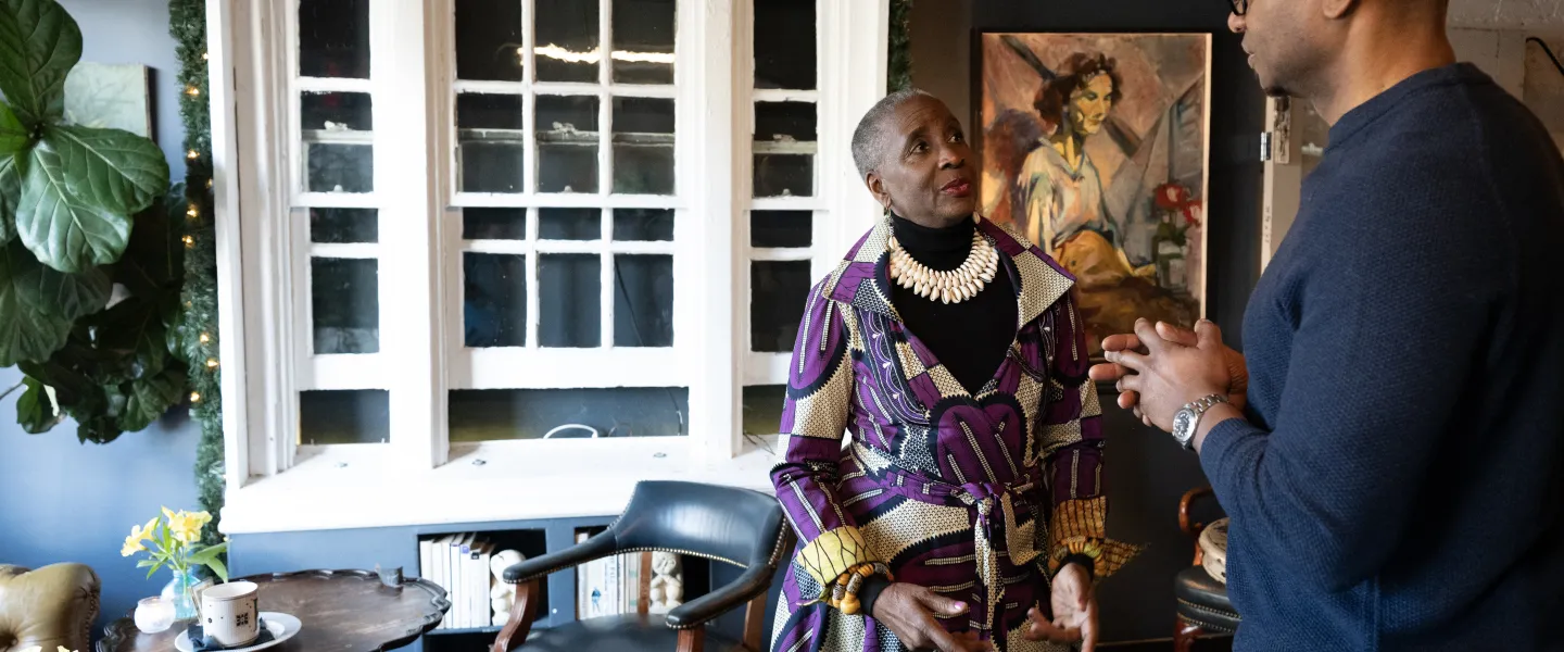 Two people have a conversation in an art-filled lounge with large windows and vintage furniture in Washington, DC.