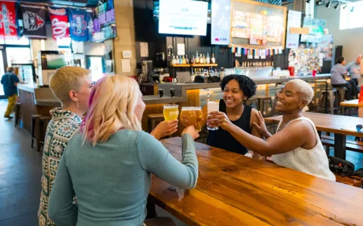 Two couples smile and clink their beers together at a brewery. 

