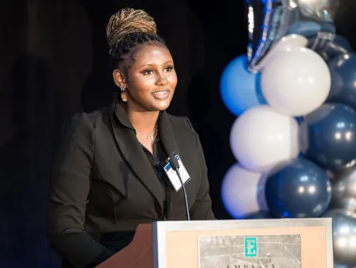 A woman speaks at a podium during an AEF scholarship event with blue and white balloon décor at an Embassy Suites venue in Washington, DC.