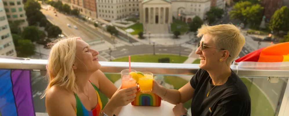A couple enjoying a cocktail on a rooftop with a view of historic city buildings below. 