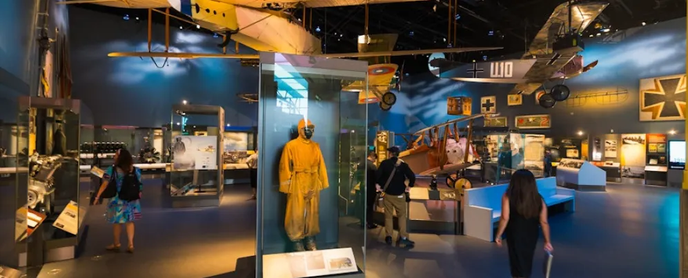 Visitors walk through an aviation exhibit with vintage aircraft and a yellow flight suit on display.
