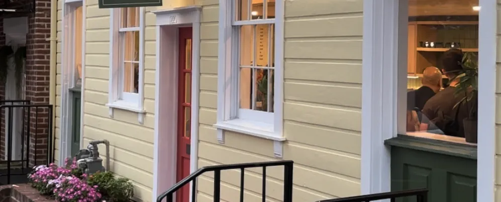 The exterior of Flor Coffee + Books, a quaint home painted yellow with inviting flowers and a red door. 