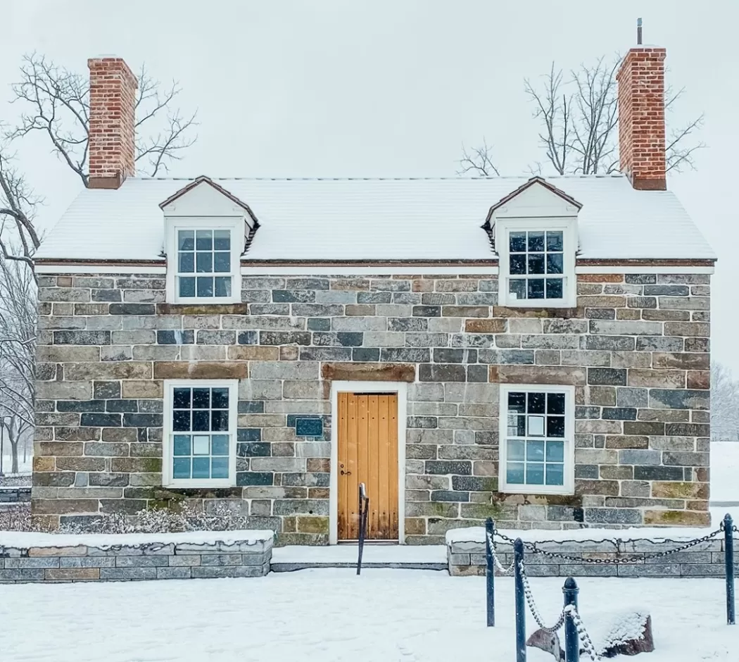 Old stone building covered in snow, with two chimneys and a old wooden door